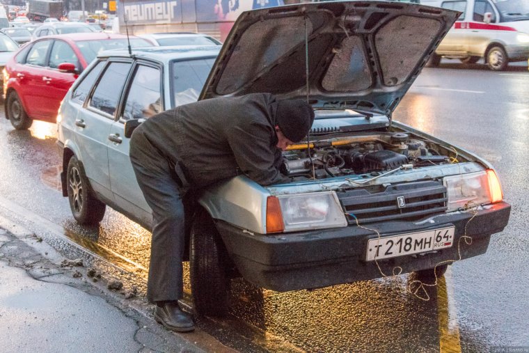 Чинит машину во дворе